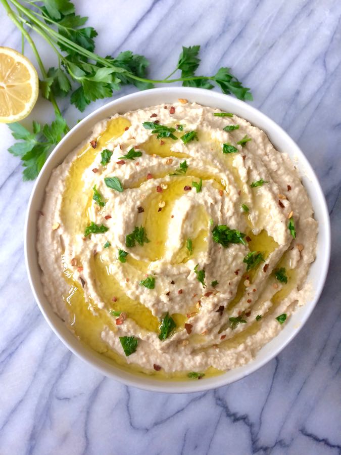 An overhead shot of a bowl of homemade hummus, drizzled with olive oil and sprinkled with parsley.