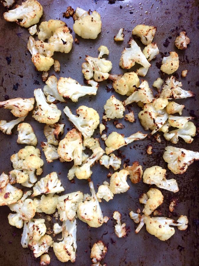 Overhead shot of a roasting pan with roasted cauliflower florets, nicely browned, scattered across it.