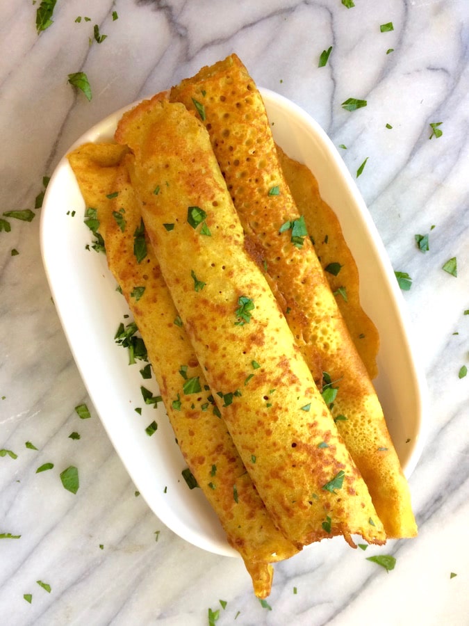 Three turmeric crepes rolled up in a dish, sprinkled with parsley.
