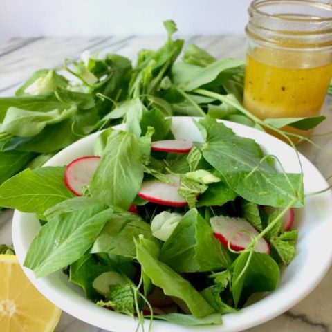 A bowl of pea shoot salad, with mint and radishes, and a jar of lemon-garlic dressing.
