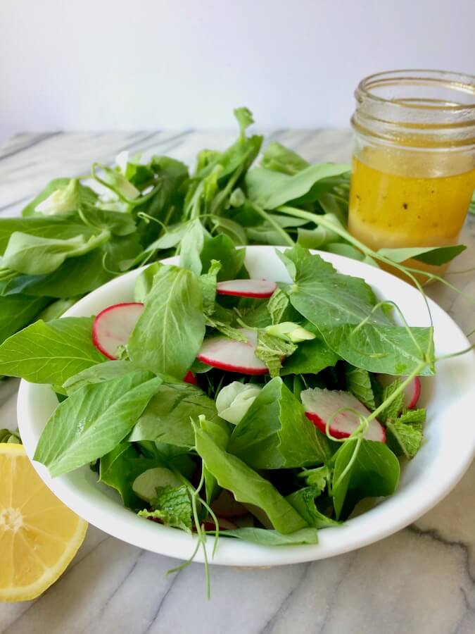 A bowl of pea shoot salad, with mint and radishes, and a jar of lemon-garlic dressing.